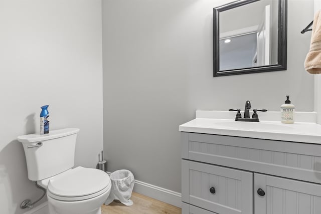 half bath with toilet, vanity, wood finished floors, and baseboards