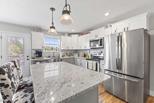 kitchen featuring light wood finished floors, a sink, light stone countertops, appliances with stainless steel finishes, and white cabinetry