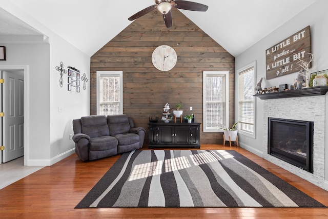 living room with a stone fireplace, wooden walls, wood-type flooring, and vaulted ceiling