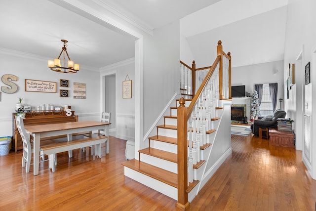 stairs with an inviting chandelier, crown molding, and wood-type flooring