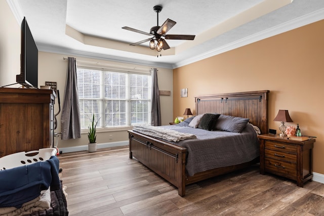 bedroom with a raised ceiling, wood-type flooring, ornamental molding, and ceiling fan