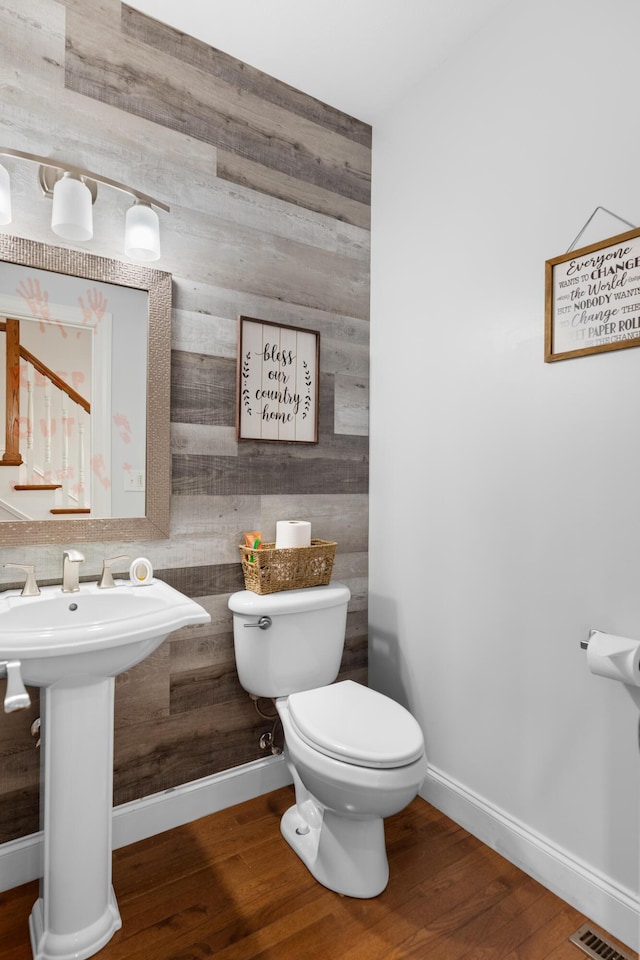 bathroom featuring hardwood / wood-style flooring, wooden walls, and toilet