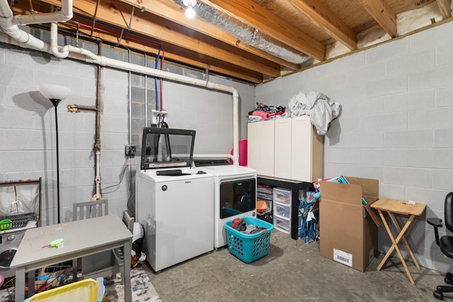 clothes washing area featuring laundry area, concrete block wall, and washing machine and clothes dryer