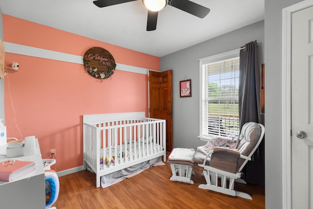 bedroom with a nursery area, ceiling fan, baseboards, and wood finished floors
