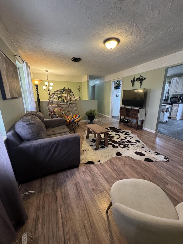 living area with visible vents, baseboards, an inviting chandelier, wood finished floors, and a textured ceiling