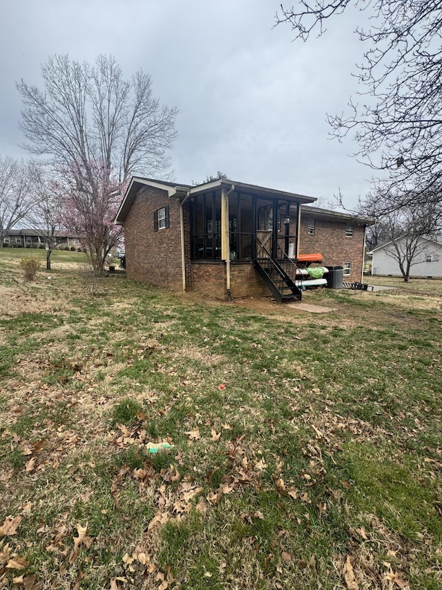 exterior space featuring brick siding, a lawn, central AC, and a sunroom