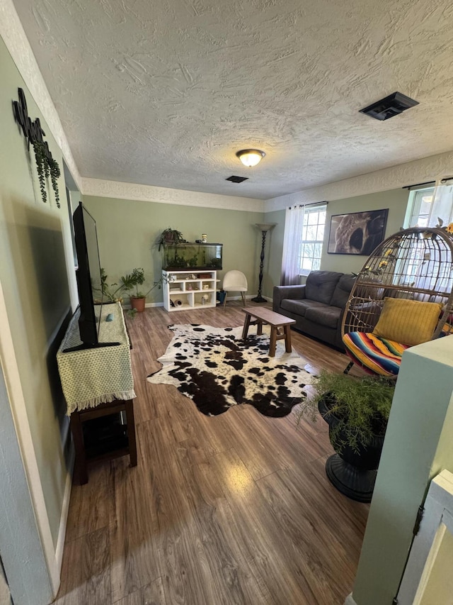 living room featuring visible vents, baseboards, a textured ceiling, and wood finished floors