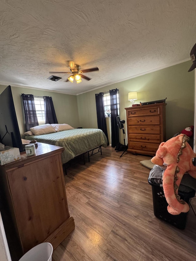 bedroom featuring a ceiling fan, wood finished floors, visible vents, a textured ceiling, and crown molding