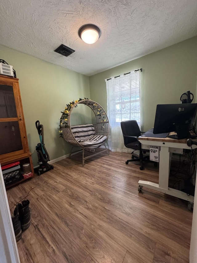 office area with visible vents, baseboards, a textured ceiling, and wood finished floors