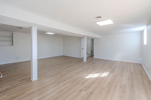 basement featuring light wood-type flooring and a textured ceiling