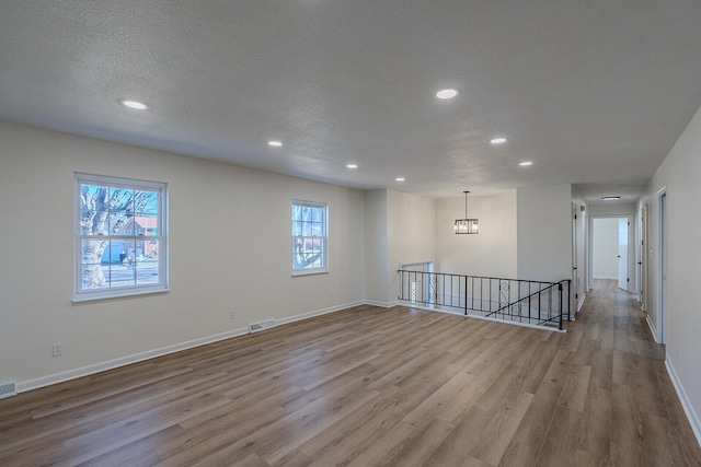 unfurnished room featuring a textured ceiling, light hardwood / wood-style flooring, and a notable chandelier