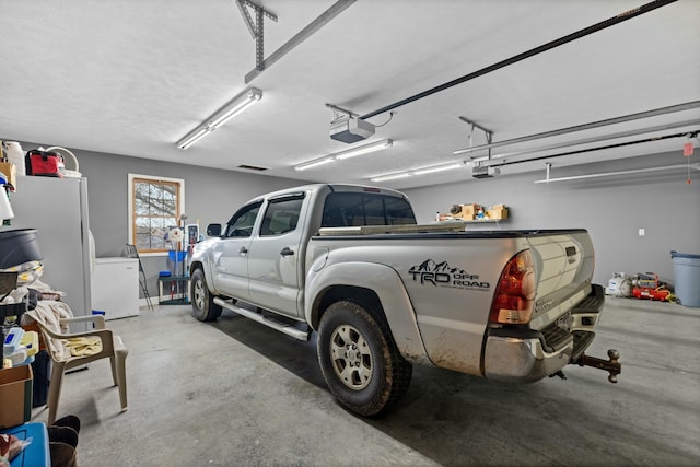 garage with white refrigerator, refrigerator, and a garage door opener