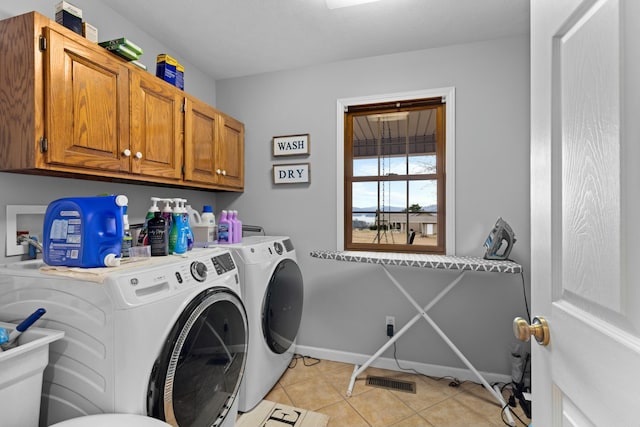 laundry room with washing machine and clothes dryer, light tile patterned floors, and cabinets