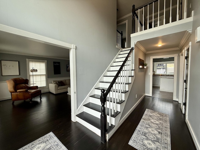 staircase featuring baseboards, a high ceiling, ornamental molding, and hardwood / wood-style flooring