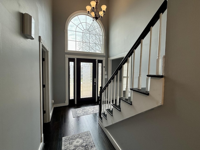 entryway featuring baseboards, dark wood finished floors, an inviting chandelier, a high ceiling, and stairs