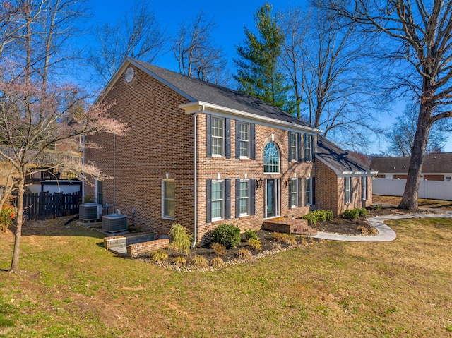 view of front facade with cooling unit, brick siding, a front yard, and fence