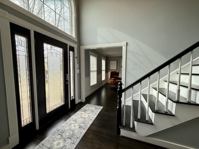 foyer entrance with ornamental molding, wood finished floors, baseboards, a towering ceiling, and stairs