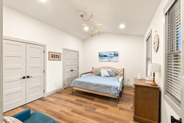 bedroom with lofted ceiling, hardwood / wood-style floors, two closets, and a notable chandelier