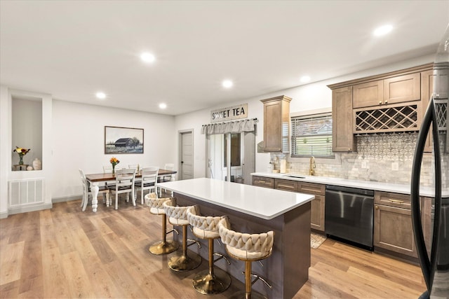 kitchen featuring sink, a kitchen island, stainless steel dishwasher, and light wood-type flooring