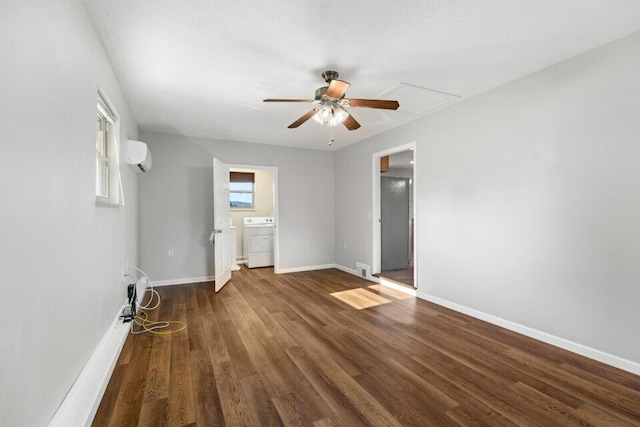 empty room featuring a wall mounted AC, attic access, washer / clothes dryer, ceiling fan, and wood finished floors