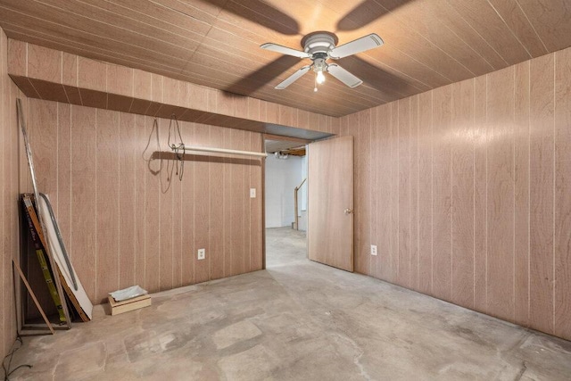 unfurnished room with concrete flooring, ceiling fan, and wood walls