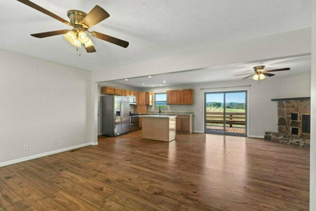 unfurnished living room featuring baseboards, dark wood-style floors, ceiling fan, and a fireplace