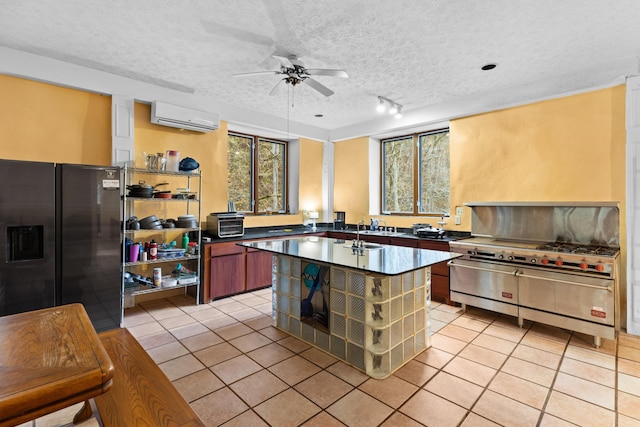 kitchen with a wall mounted air conditioner, black fridge, a textured ceiling, stainless steel stove, and light tile patterned flooring