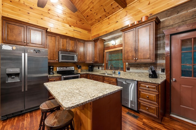 kitchen featuring dark hardwood / wood-style flooring, sink, appliances with stainless steel finishes, a kitchen island, and wood walls