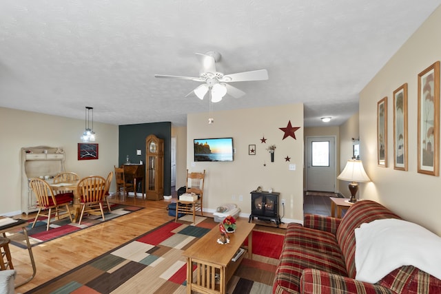 living room with ceiling fan, wood-type flooring, a textured ceiling, and a wood stove