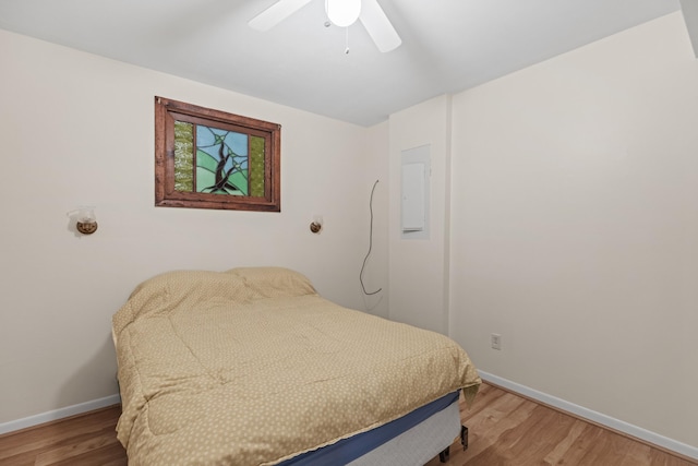 bedroom featuring light wood finished floors, baseboards, electric panel, and a ceiling fan