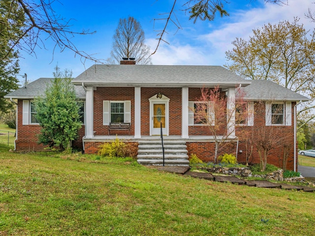 view of front facade with a front lawn, a chimney, covered porch, and brick siding