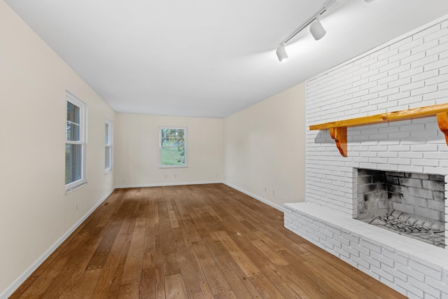 unfurnished living room featuring wood-type flooring, a brick fireplace, track lighting, and baseboards