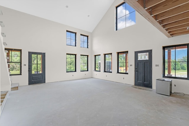 unfurnished living room featuring beamed ceiling, a healthy amount of sunlight, and a high ceiling