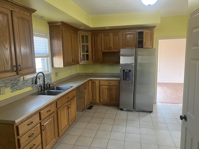 kitchen with a sink, open shelves, stainless steel fridge, and brown cabinetry