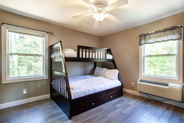 bedroom featuring hardwood / wood-style floors, multiple windows, and an AC wall unit