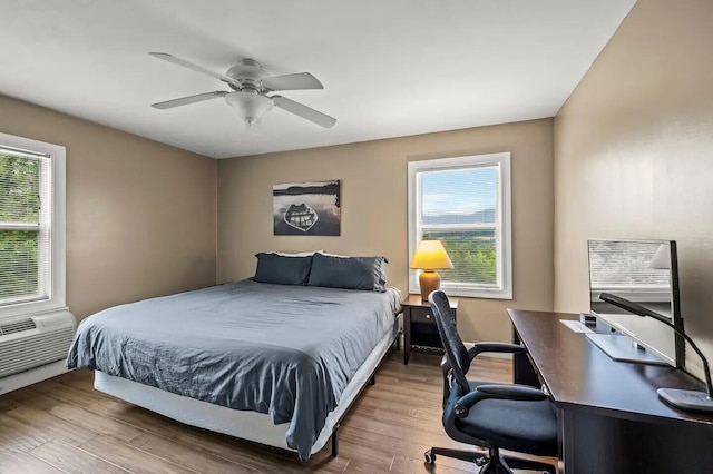 bedroom with a wall mounted air conditioner, hardwood / wood-style floors, and ceiling fan