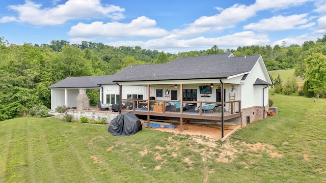 rear view of house with ceiling fan, a lawn, a deck, and roof with shingles