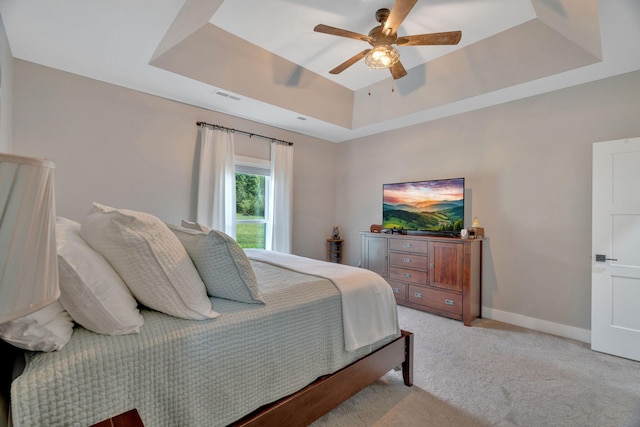 bedroom featuring a tray ceiling, light colored carpet, ceiling fan, and baseboards