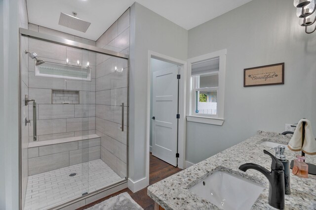 full bath featuring wood finished floors, a shower stall, baseboards, and double vanity