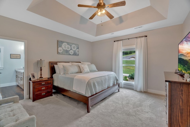 carpeted bedroom with a raised ceiling, baseboards, connected bathroom, and a ceiling fan