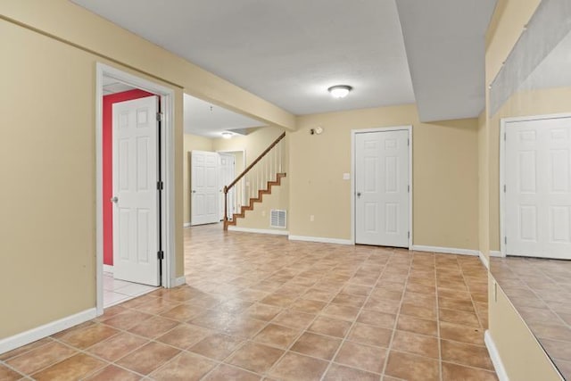 finished basement featuring baseboards, stairway, light tile patterned floors, and visible vents
