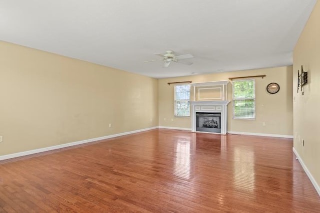 unfurnished living room with a fireplace, ceiling fan, baseboards, and wood finished floors
