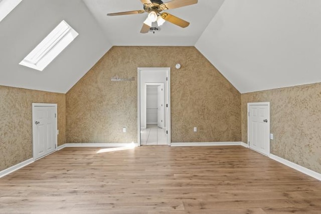additional living space with wood finished floors, a ceiling fan, and vaulted ceiling with skylight