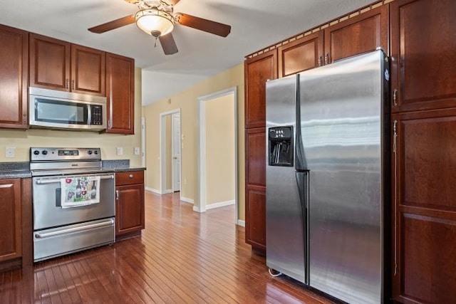 kitchen featuring baseboards, dark wood-style flooring, ceiling fan, dark countertops, and stainless steel appliances