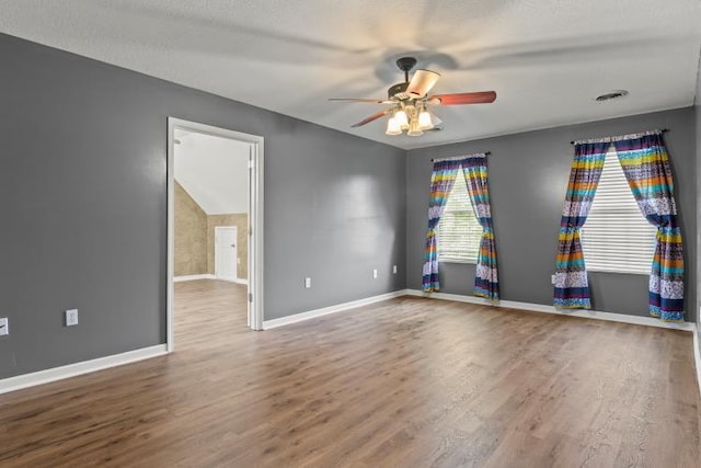 empty room with visible vents, wood finished floors, baseboards, and ceiling fan
