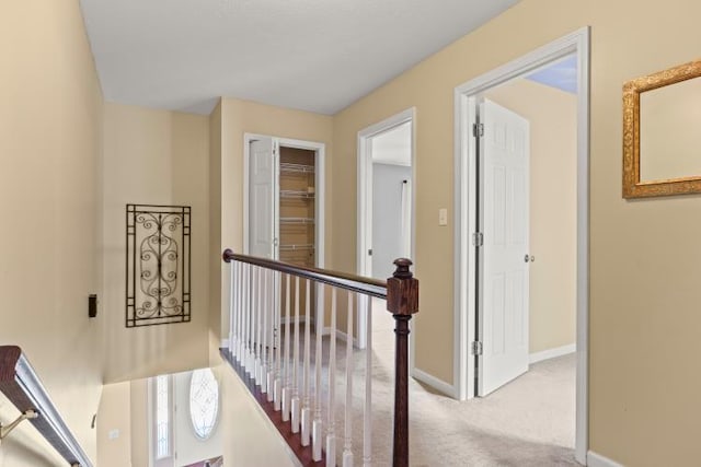 hall with an upstairs landing, baseboards, and carpet floors