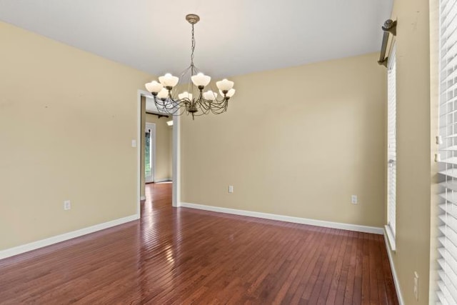 spare room featuring baseboards, a notable chandelier, and dark wood finished floors