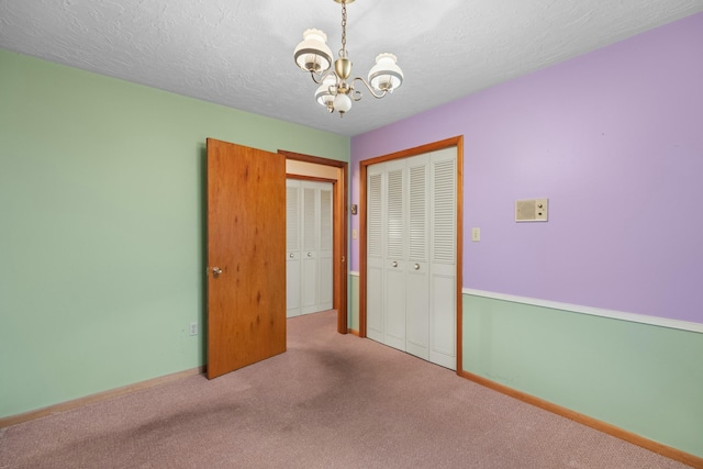 unfurnished bedroom featuring a closet, baseboards, a textured ceiling, carpet, and a notable chandelier