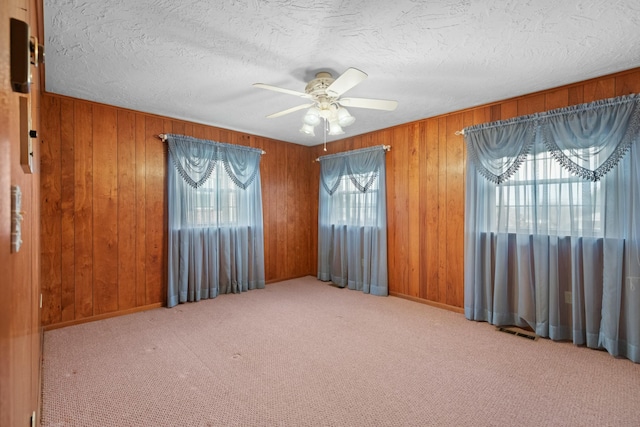 carpeted spare room featuring ceiling fan, a textured ceiling, visible vents, baseboards, and wooden walls