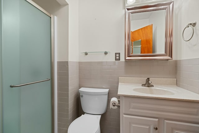 bathroom with tile walls, a shower with shower door, a wainscoted wall, vanity, and toilet